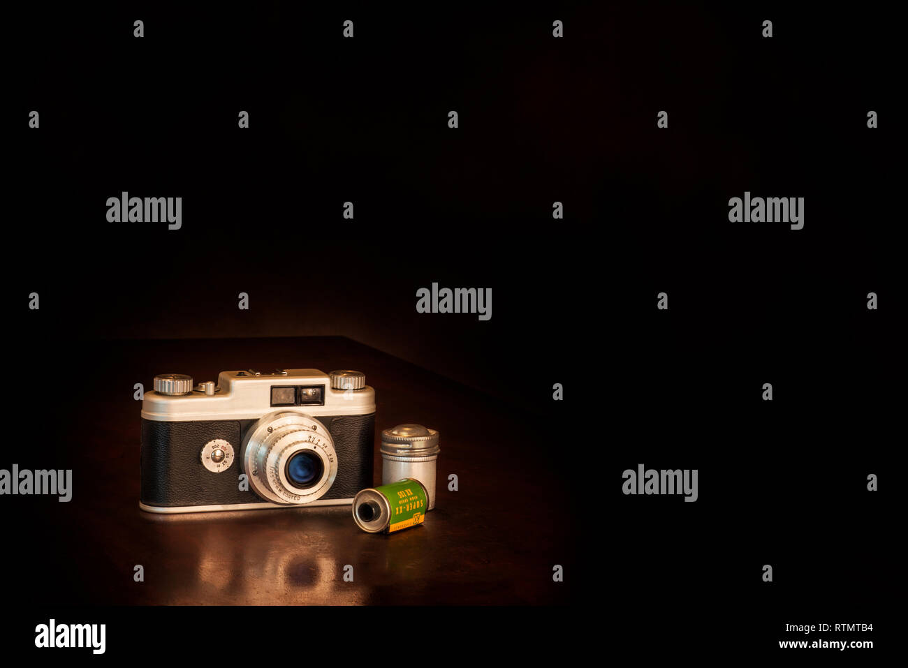 Inquadratura orizzontale di un vecchio 50's fotocamera e film su uno sfondo marrone con copia spazio. La riflessione parziale della telecamera sul piano portapaziente. Foto Stock