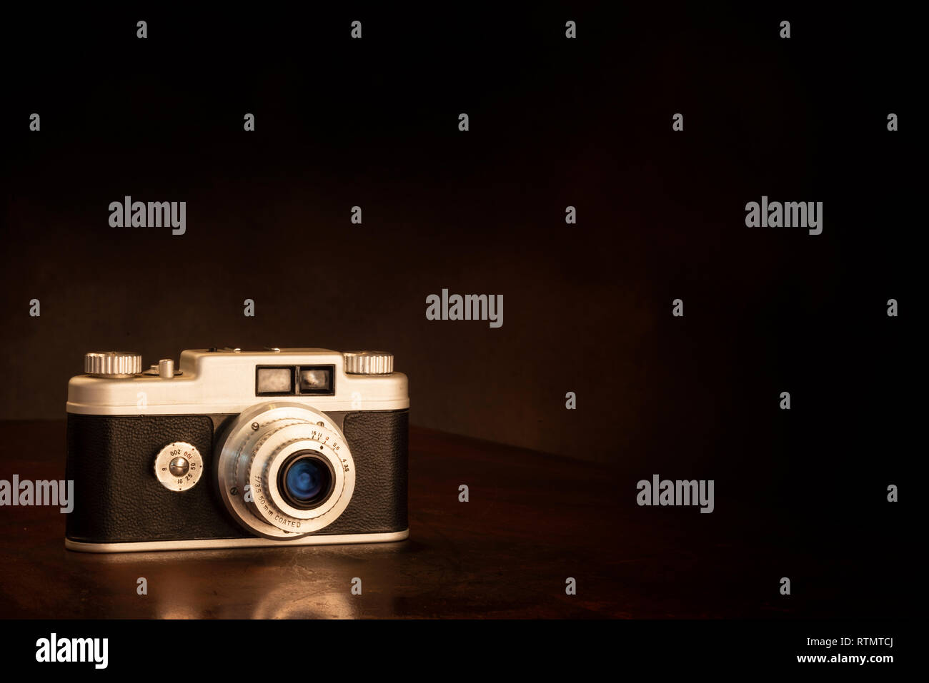 Inquadratura orizzontale di una vecchia macchina fotografica da 35mm su uno sfondo marrone con copia spazio. La riflessione parziale della telecamera sul piano portapaziente. Foto Stock