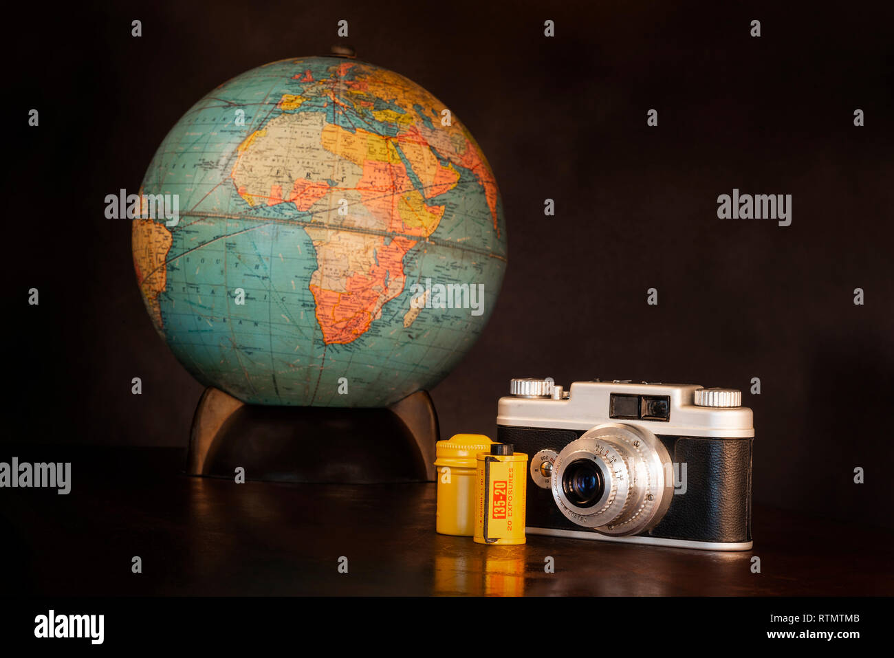 Inquadratura orizzontale di una fotocamera vintage, film, giallo barattolo metallico e globo mondo su uno sfondo marrone con copia spazio. Foto Stock