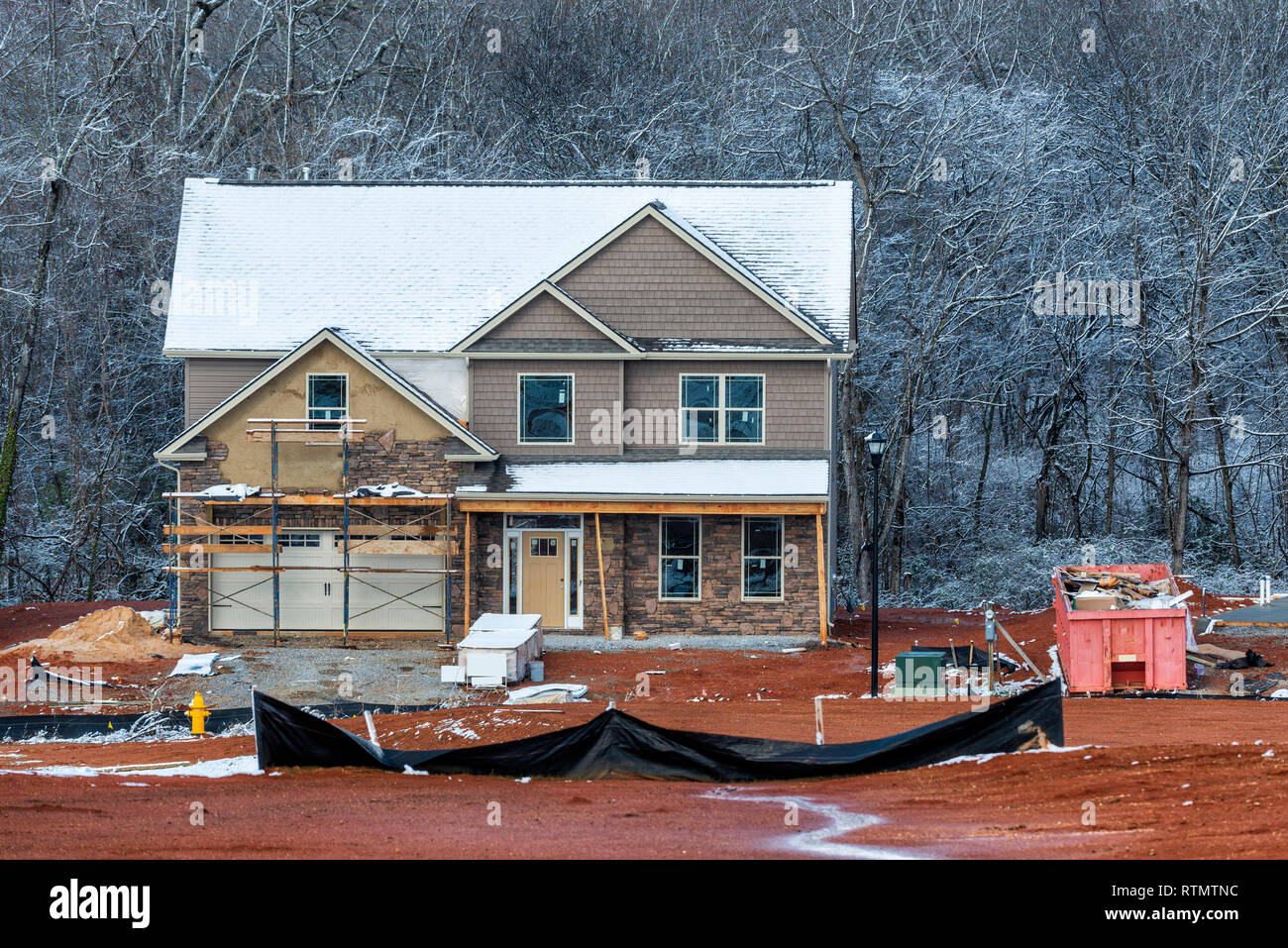 Inquadratura orizzontale di un inverno di due-storia home sito in costruzione. C'è la neve sul tetto e gli alberi dietro la casa in costruzione. Foto Stock