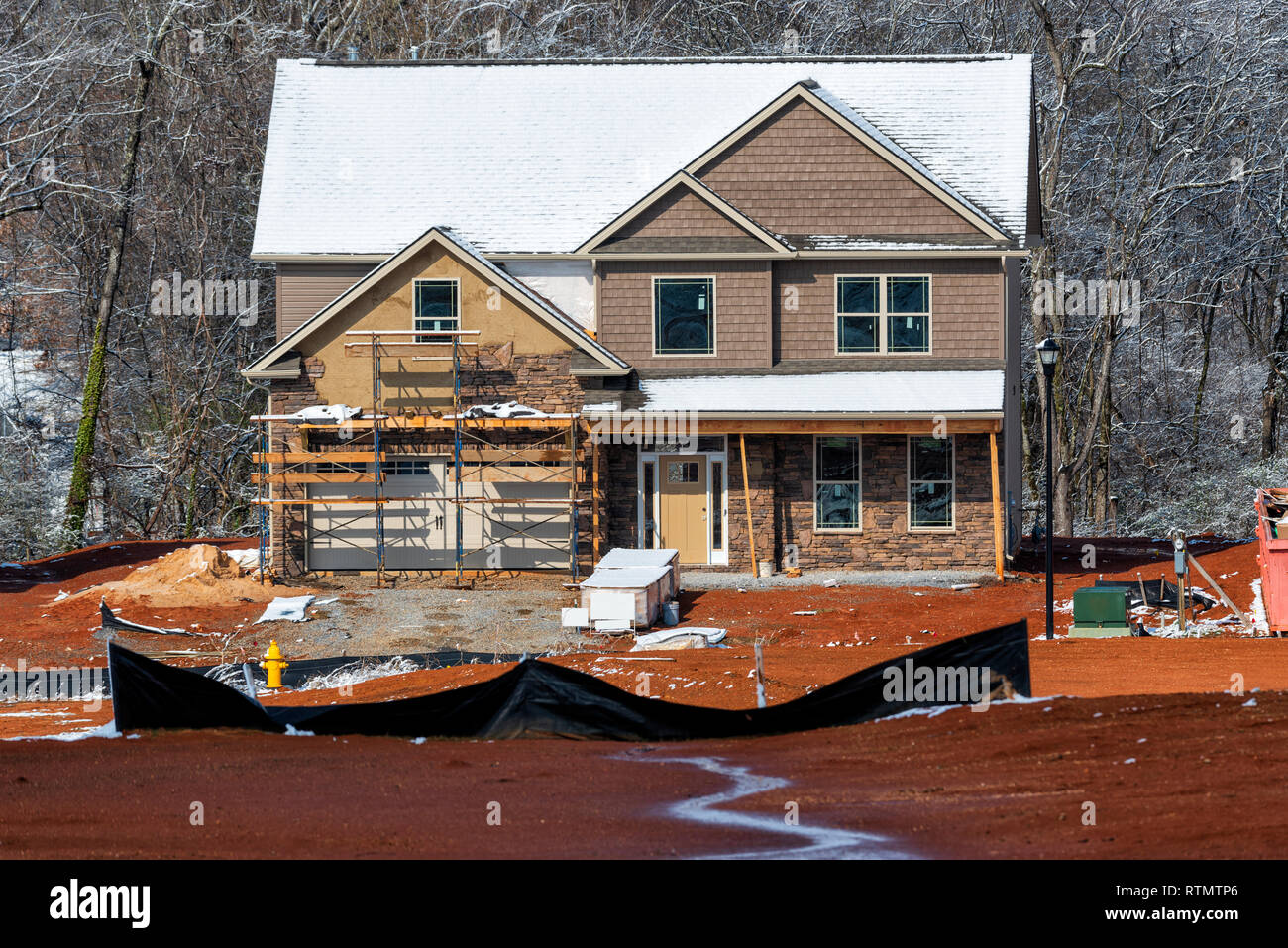 Inquadratura orizzontale di un inverno di due-storia home sito in costruzione. C'è la neve sul tetto e gli alberi dietro la casa in costruzione. Foto Stock