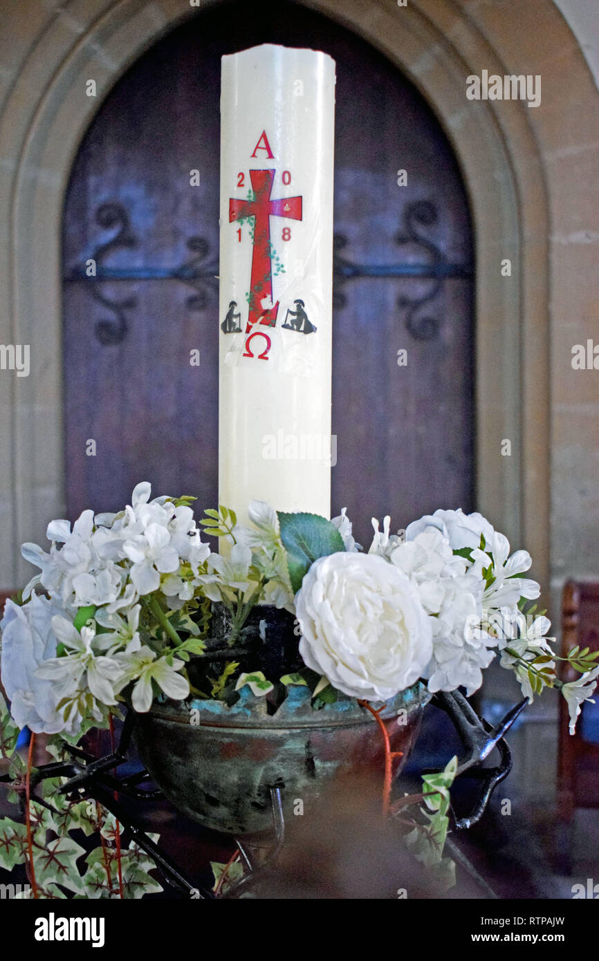 Una candela di colore bianco con una croce rossa su di esso in un bianco floreale davanti a un legno marrone porta della chiesa Foto Stock