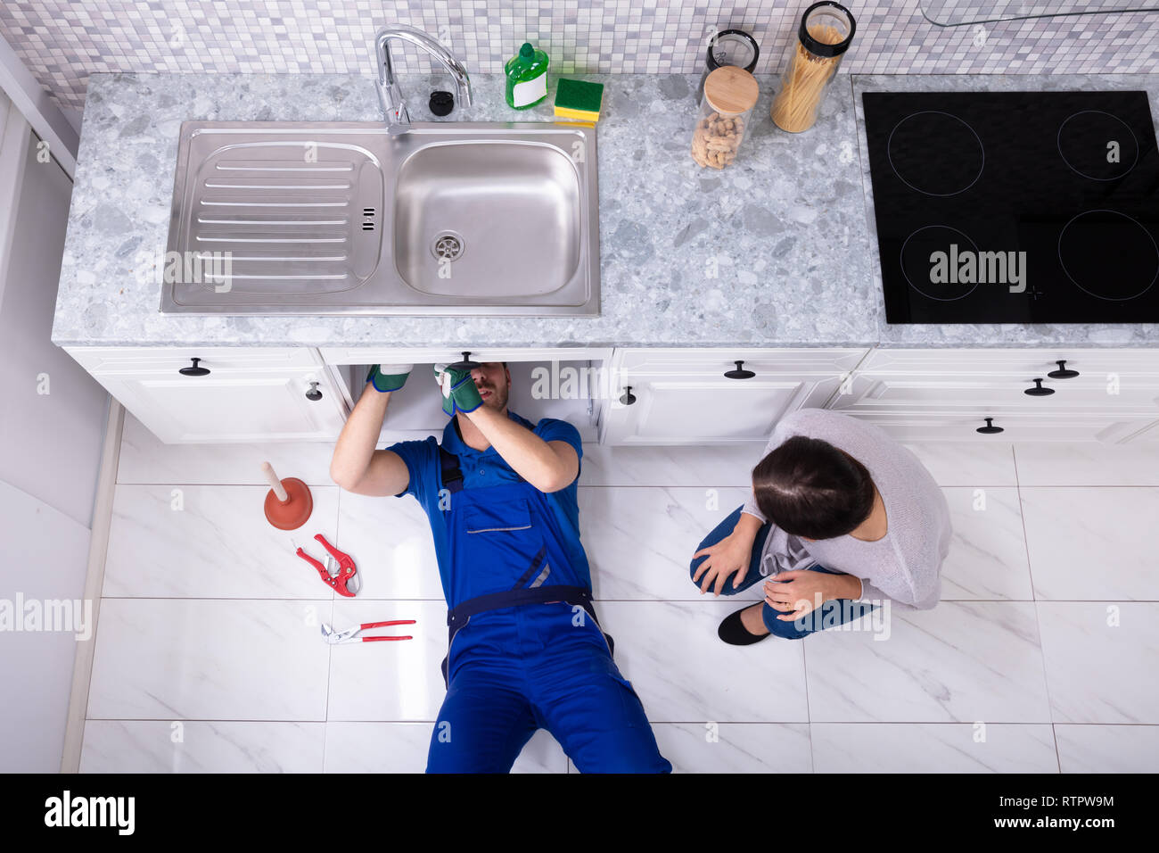 Elevato angolo di visione della donna che guarda tuttofare giacente sul piano di riparazione lavello in cucina Foto Stock