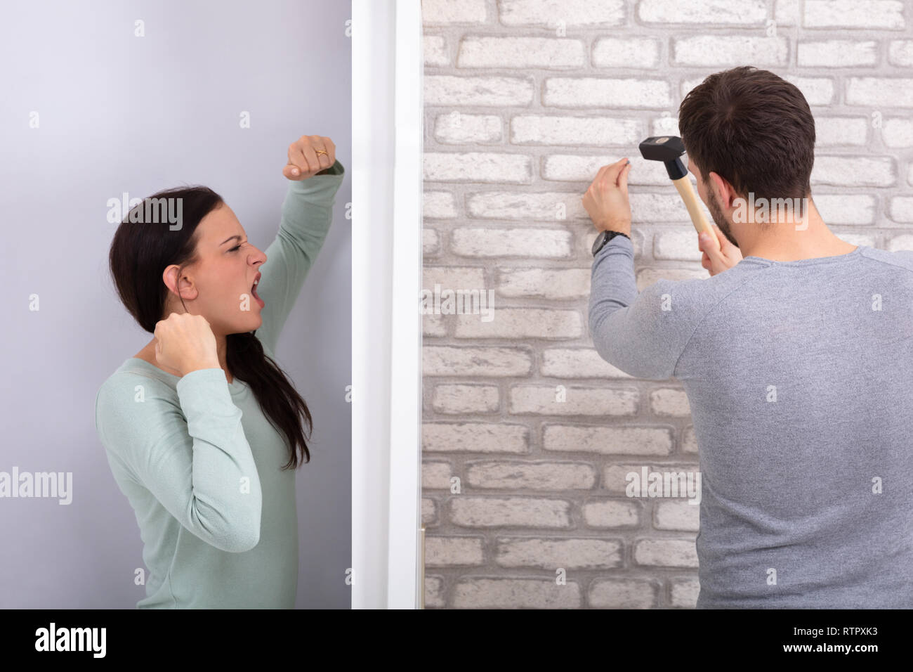 Una donna arrabbiato grida dietro la parete con il prossimo uomo che colpisce il muro di mattoni Foto Stock
