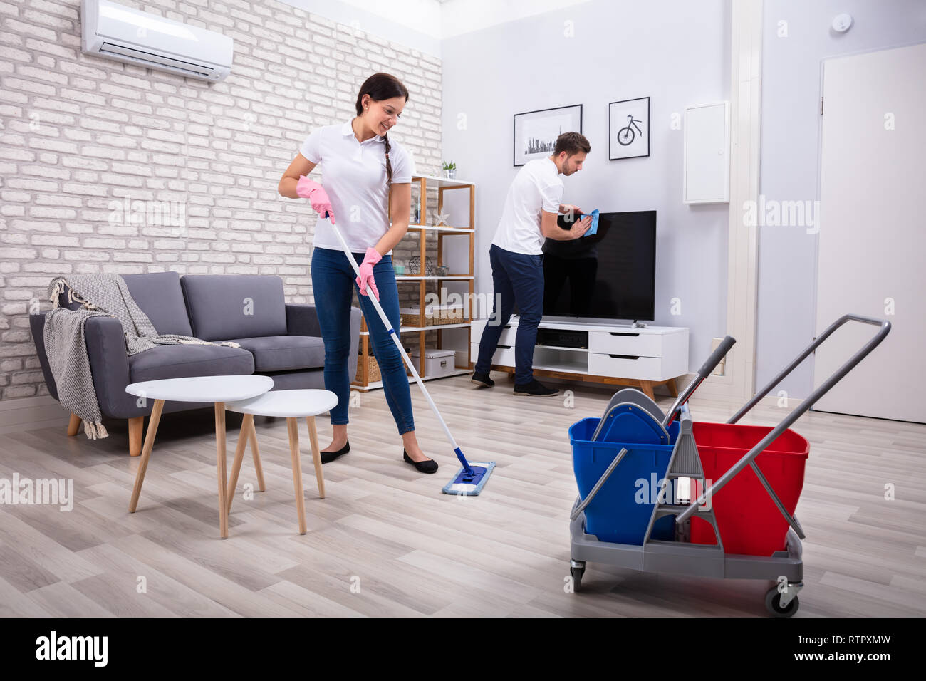I giovani lavoratori della televisione di pulizia e il pavimento con Mop e spugna a casa Foto Stock