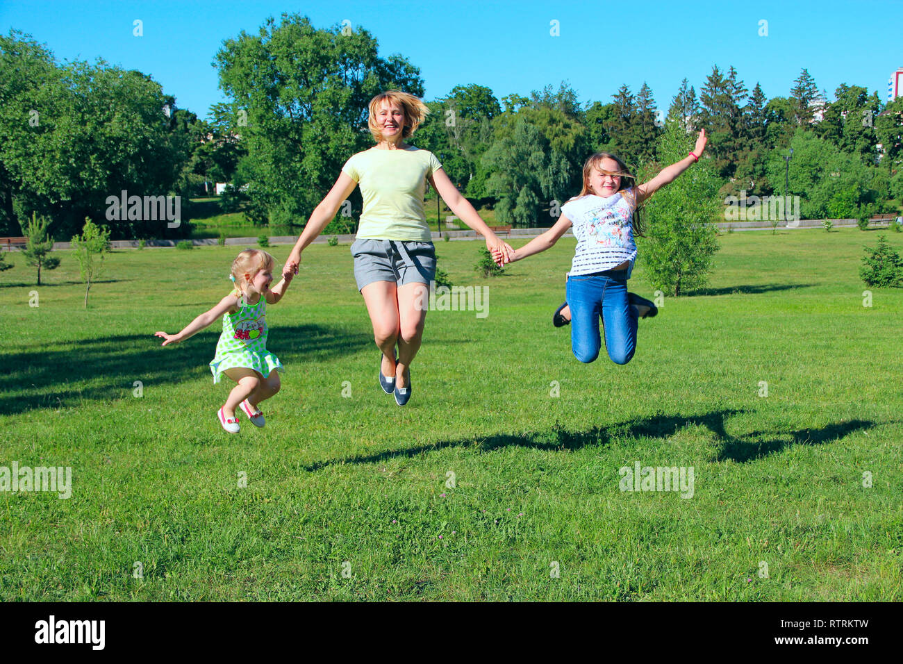 Felice madre divertirsi saltando con le sue figlie sull'erba verde. La famiglia felice team. Famiglia godendo le vacanze estive. Le persone che si godono la vacanza con la famiglia Foto Stock