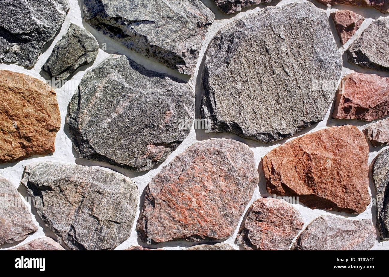 Pietre di diverse dimensioni, forme e colori su un lato esterno della parete di roccia Foto Stock