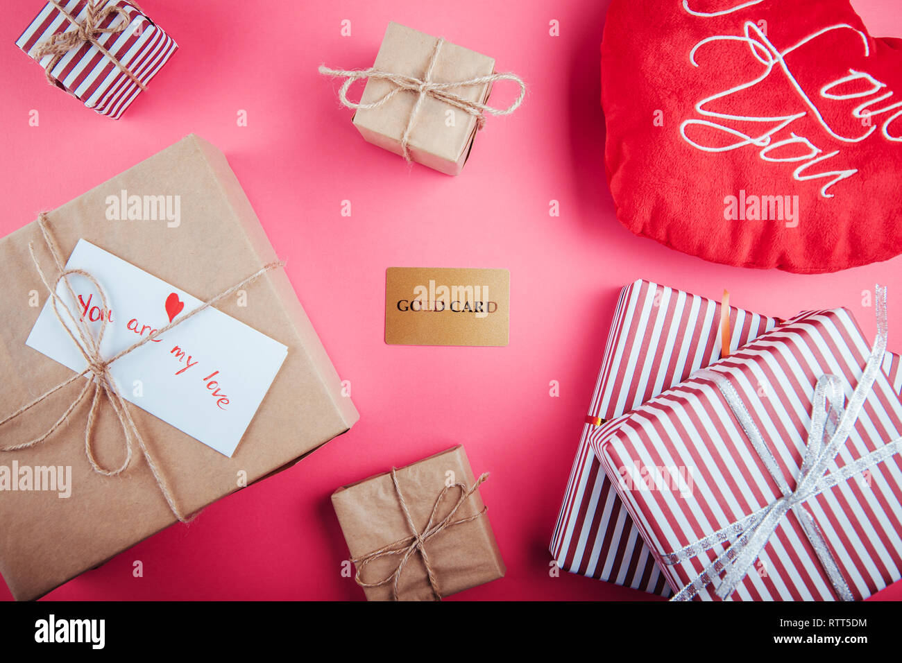 Acquistare i regali per il giorno di San Valentino con una carta oro. Confezioni regalo e cuore cuscino su sfondo rosa Foto Stock