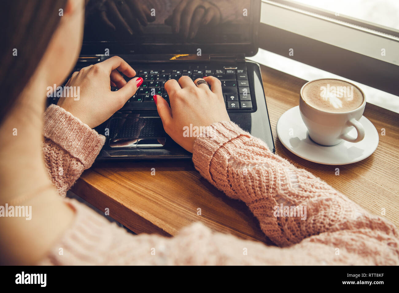 Giovani freelancer gode di caffè nella caffetteria usando un computer portatile nella parte anteriore della finestra Foto Stock