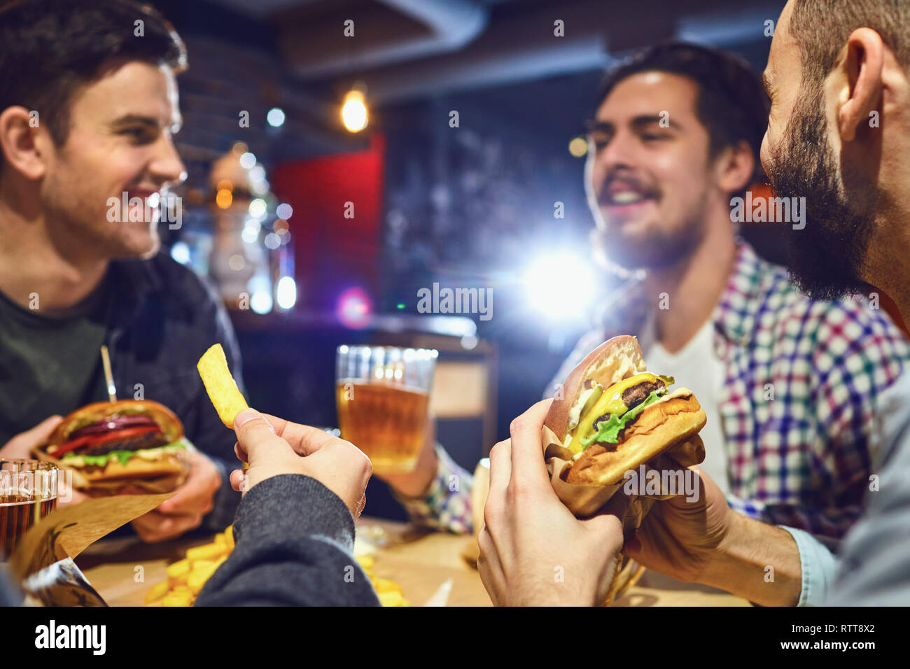 Happy amici mangiare hamburger, bere birra in un bar. Foto Stock