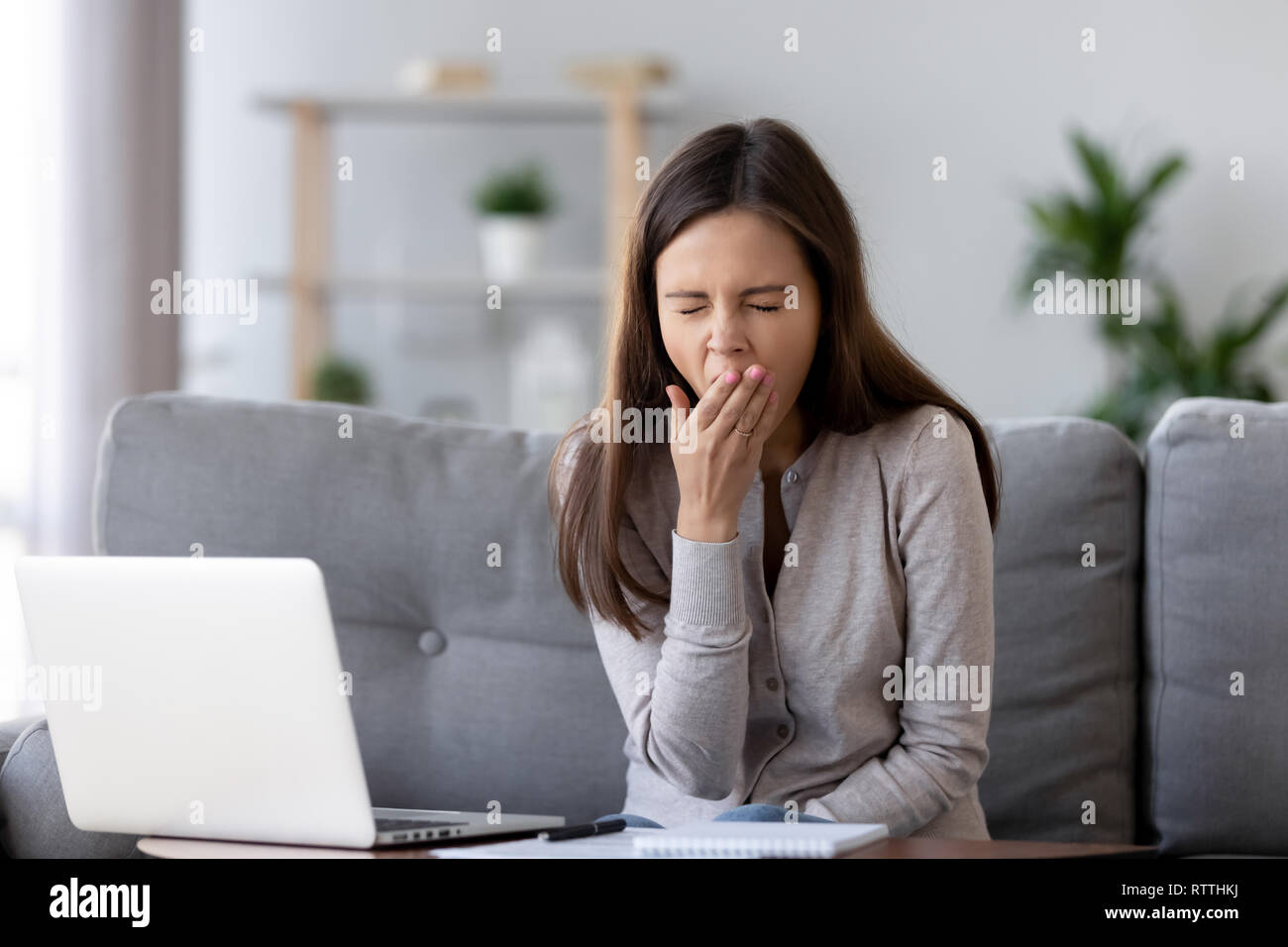 Stanco donna sbadigli, seduta a tavola con laptop, pigro al lavoro Foto Stock