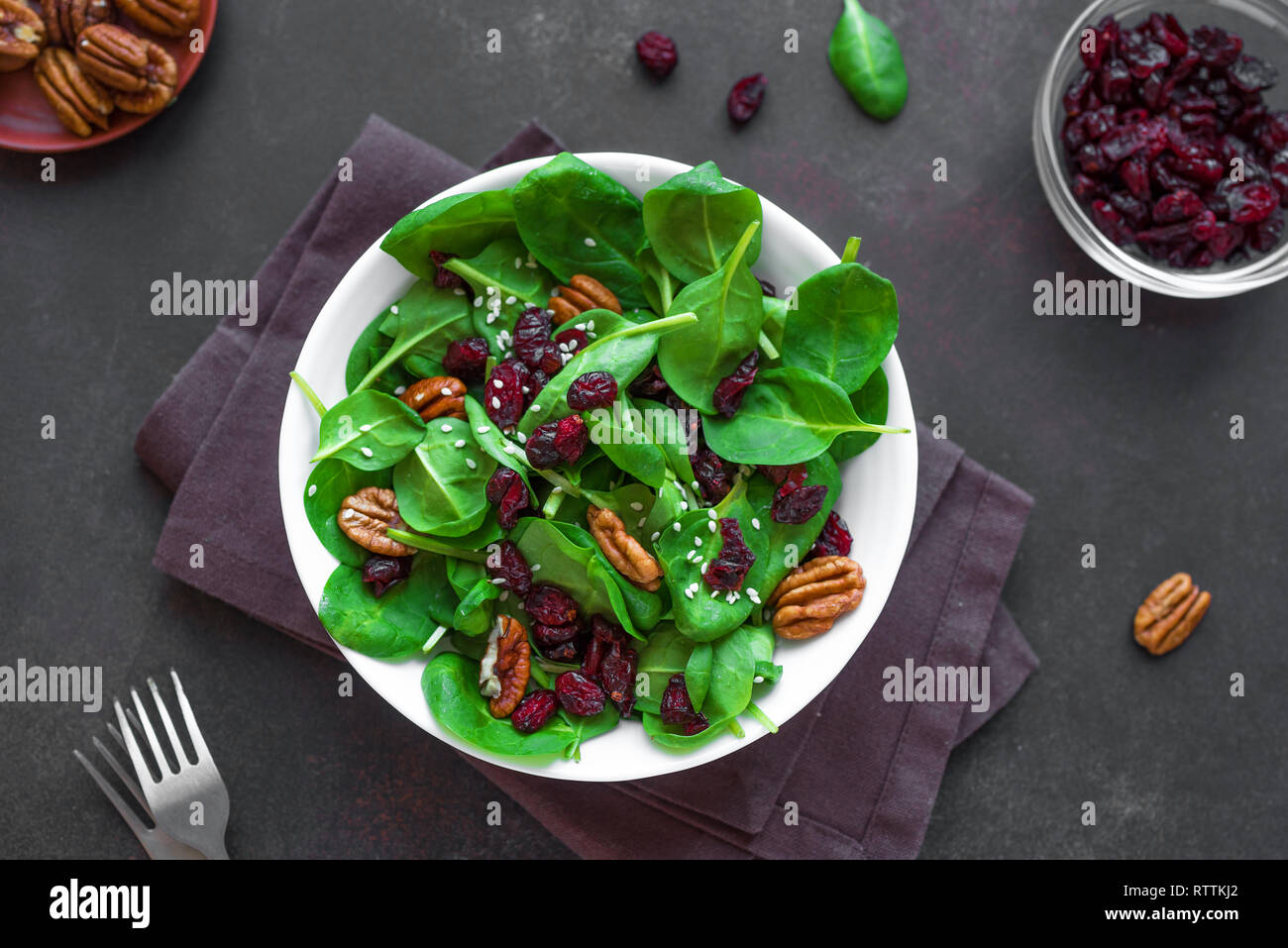 Insalata di spinaci con noci pecan e mirtilli rossi secchi su sfondo nero, vista dall'alto. Pulire Heathy vegan cibi crudi, insalata fresca. Foto Stock