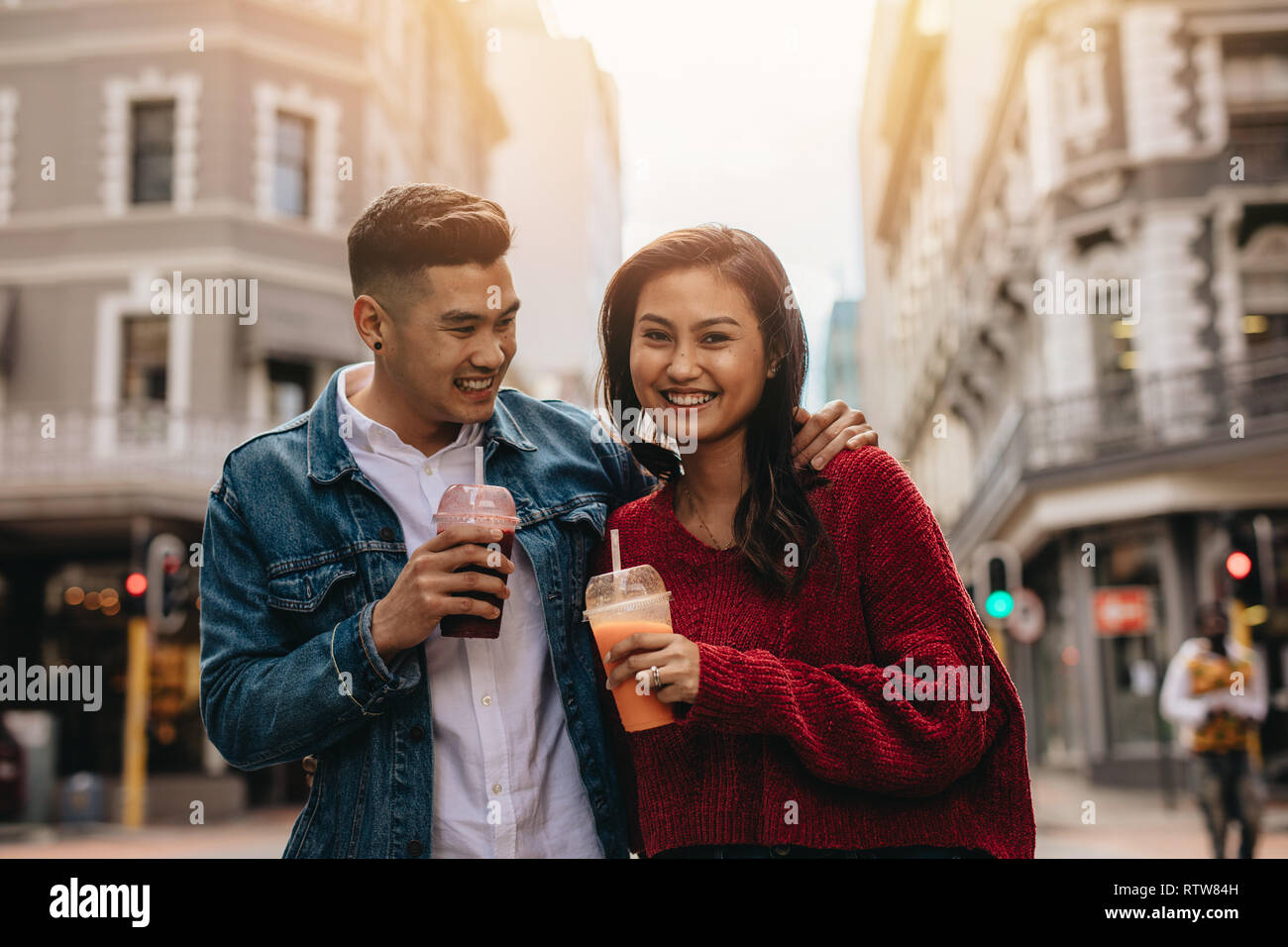 Giovani asiatici giovane camminando sulla strada di città con del succo di frutta fresco. Felice giovane uomo e donna su una strada di città con succo. Foto Stock
