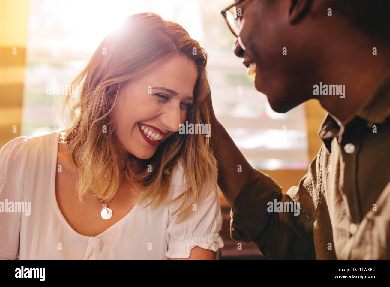 Donna sorridente sul data con il suo amore il mio ragazzo al cafe. Razza mista giovane seduti insieme presso la caffetteria con la luce solare diretta dal retro. Foto Stock