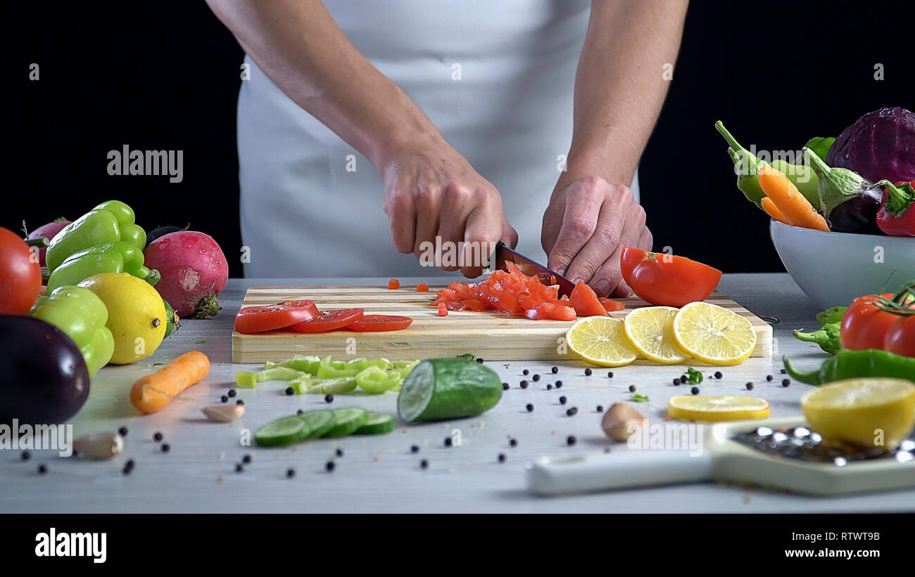 L uomo è il taglio di vegetali in cucina, affettare il pomodoro Foto Stock