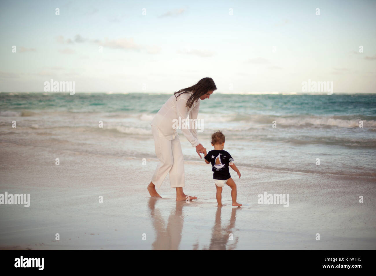 Tramonto sulla spiaggia di sabbia di madre e bambino più piccolo esplora l'oceano Foto Stock