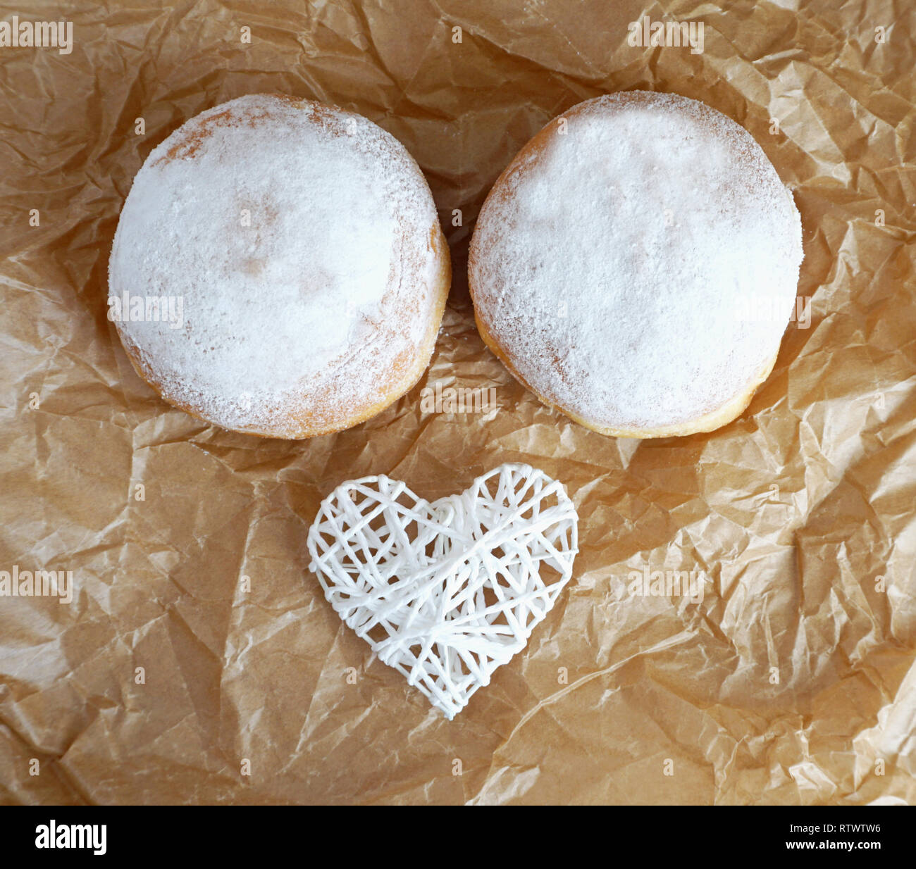 Due confetti ciambelle decorate con un bianco di cuore in marrone carta da forno vista superiore, strano concetto di cucina a vista Foto Stock