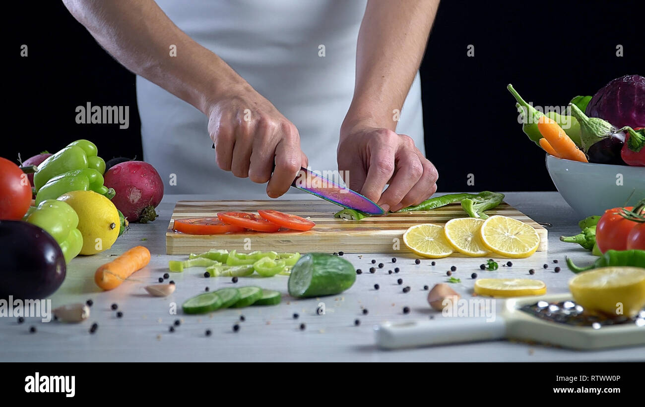 L uomo è il taglio di vegetali in cucina, affettare il peperone verde Foto Stock