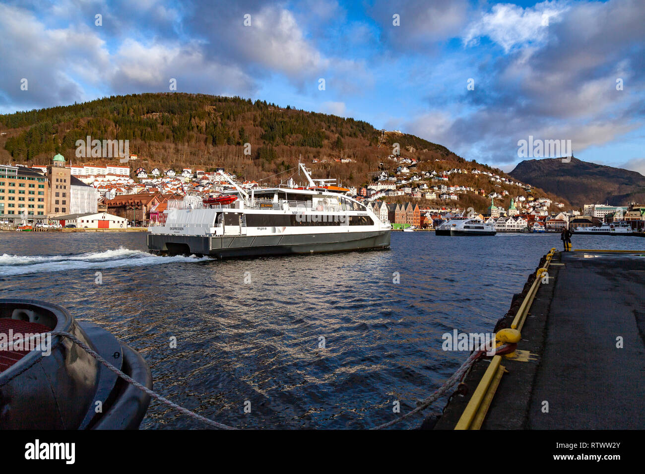 Ad alta velocità per i passeggeri Ekspressen catamarano che arrivano nel porto di Bergen, Norvegia. Sale riunioni in uscita Admiralen catamarano. Il Monte Floyen e Ulriken in t Foto Stock