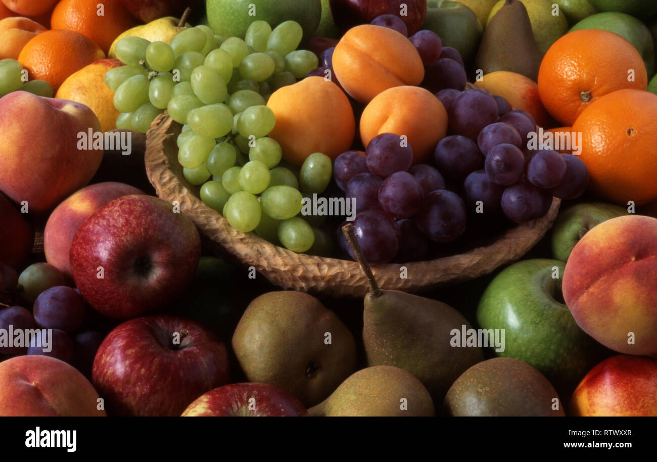 CESTINO DI UVA E ALBICOCCHE CIRCONDATO DA FRUTTA FRESCA ASSORTITA. Foto Stock