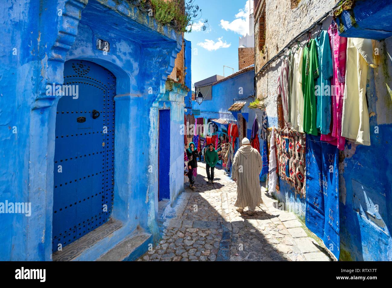 Nativo di marocchini in Djellaba, vestiti su una casa blu a parete, stretto vicolo, medina di Chefchaouen, Chaouen, Tanger-Tétouan Foto Stock