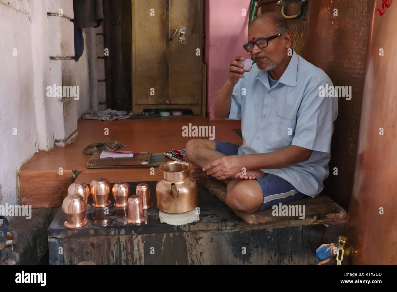 Un uomo libero di erogazione di acqua potabile da un pozzo in Javeri area Bazar, Mumbai, India, avente un tea break con un cosiddetto "taglio" (mezza tazza di tè) Foto Stock