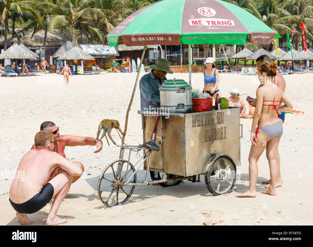 NAM TIEN, VIETNAM - Febbraio 16, 2018: cibi e bevande venditore con una scimmia circondato dai turisti in una spiaggia di sabbia in Nam Tien, Vietnam Foto Stock