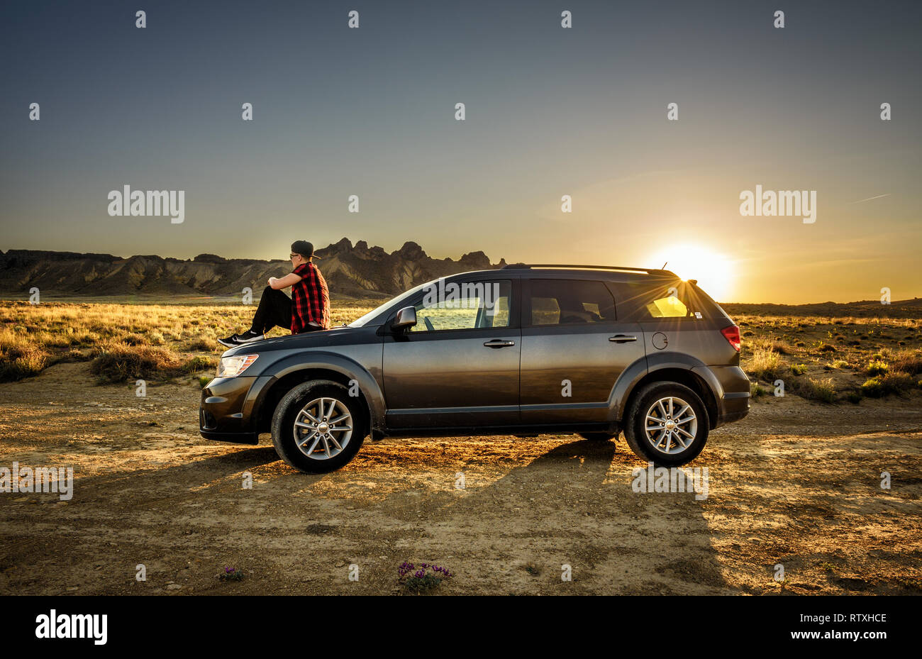 Ragazzo gode il tramonto seduti sul cofano della sua auto Foto Stock