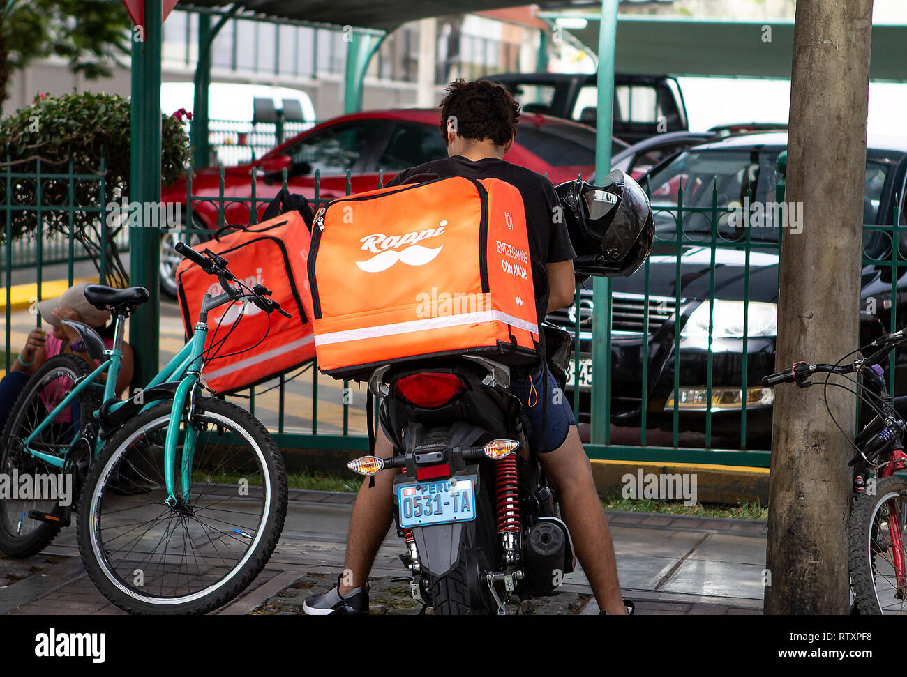 Lima, Perù - 17 Febbraio 2019: guidatore giovane ragazzo che lavora per Rappi una consegna del cibo, servizio parcheggiato al di fuori di un parcheggio. Condivisione di economia collaborativa Foto Stock