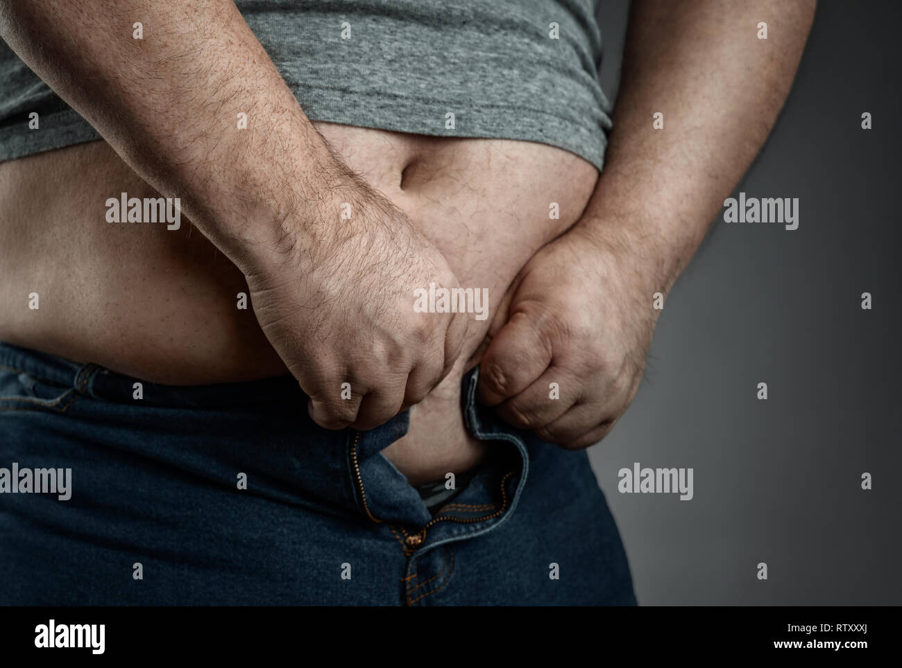 Concetto di obesità, ravvicinata di un uomo sovrappeso cercando di usura troppo piccola jeans Foto Stock