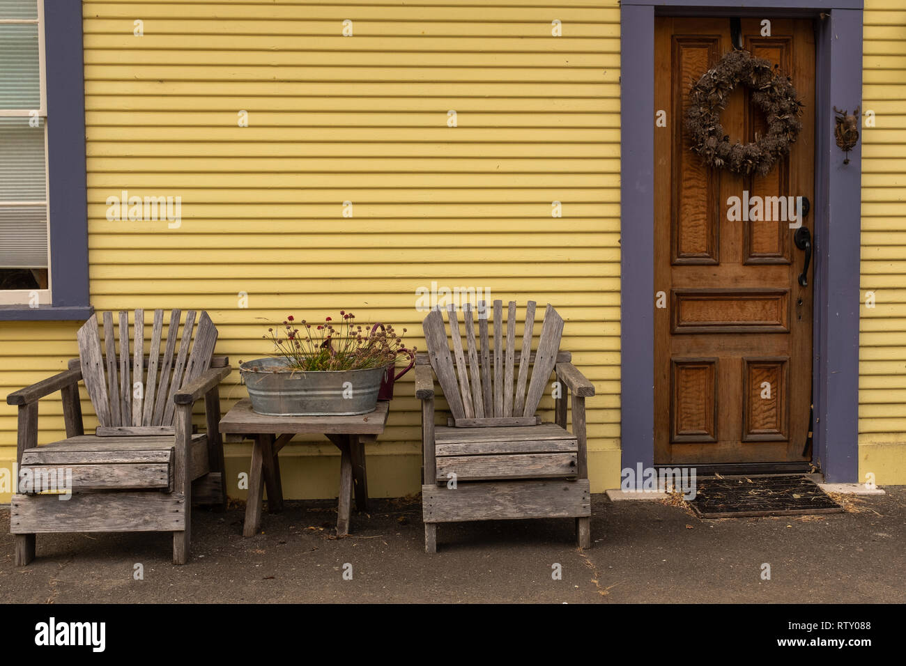 Una coppia di sedie a spiovente fuori la parte anteriore di un dipinto di giallo casa con una corona sulla porta. Foto Stock