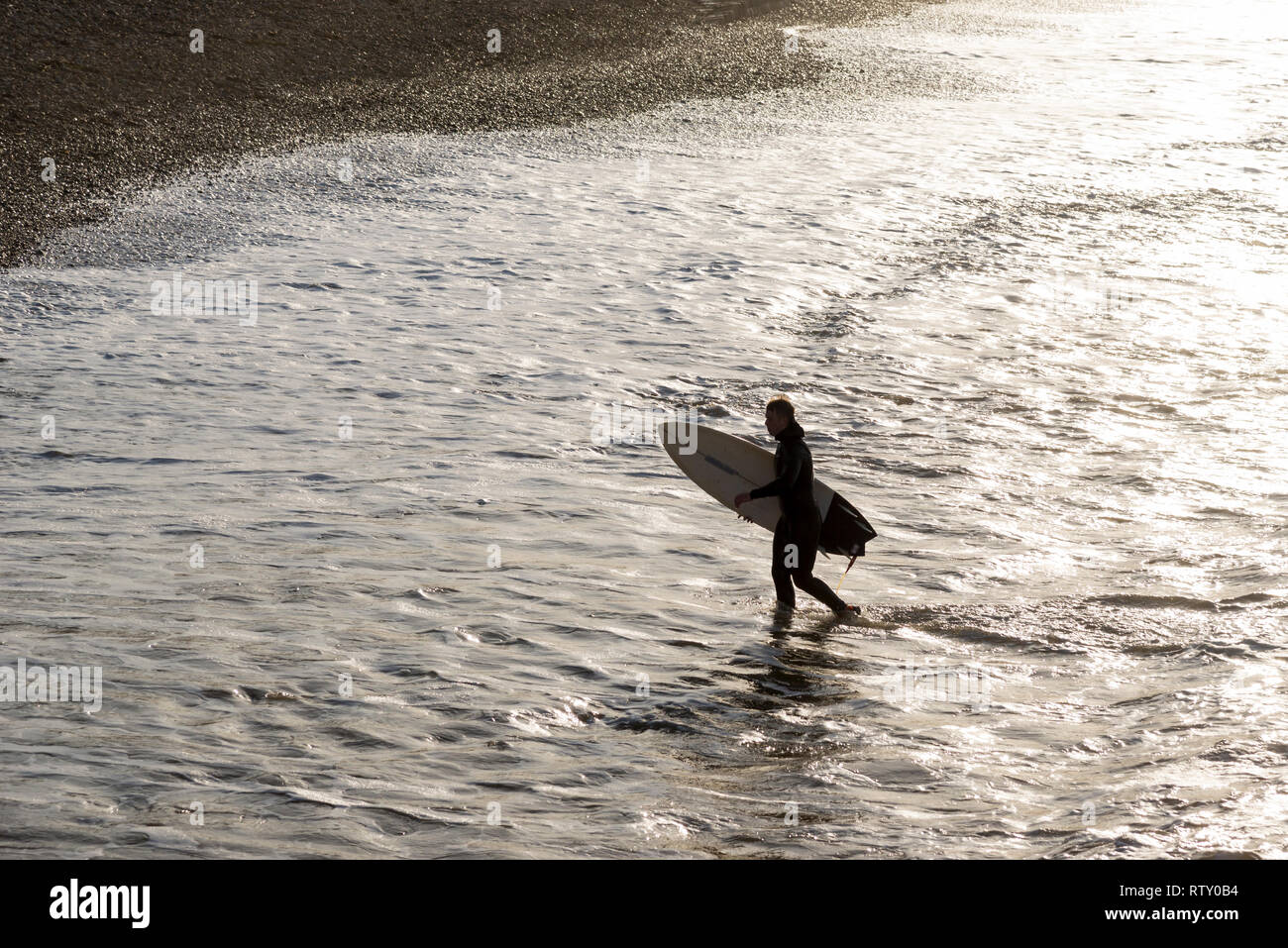 Giovane maschio surfer passeggiate fuori le onde a cambs, North Yorkshire, Inghilterra. Foto Stock