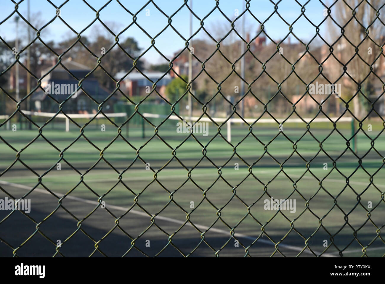 Una catena collegamento recinto nel punto focale in primo piano con un unfocused campo da tennis in background Foto Stock