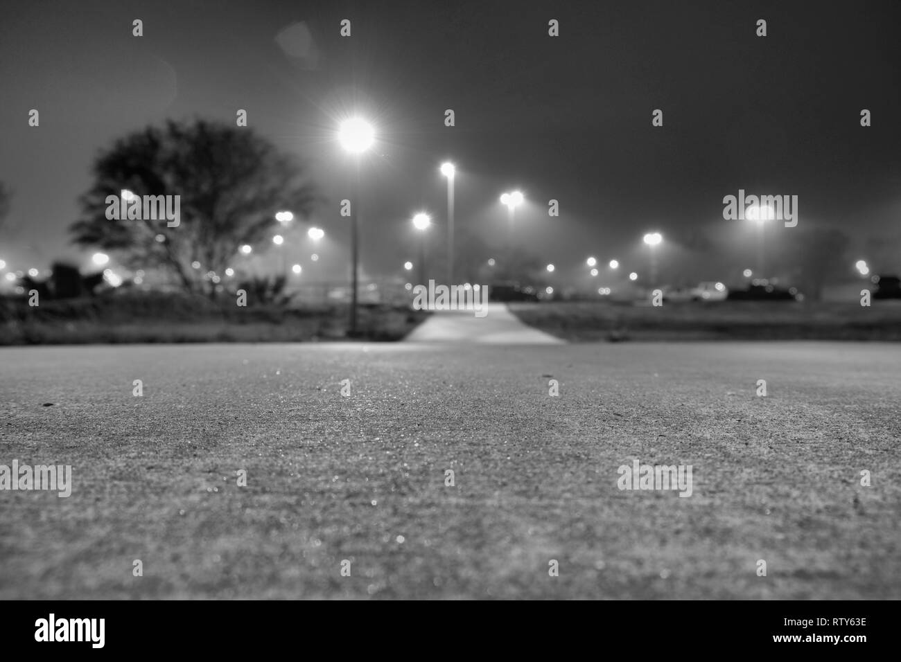 Basso in prospettiva di una passerella di cemento con lampioni causando lens flare; concentrarsi sulla immediata spazio nella parte anteriore della lente; College Station, Texas, Stati Uniti d'America. Foto Stock Basso in prospettiva di una passerella di cemento con lampioni causando lens flare; concentrarsi sulla immediata spazio nella parte anteriore della lente; College Station, Texas, Stati Uniti d'America. Foto Stock