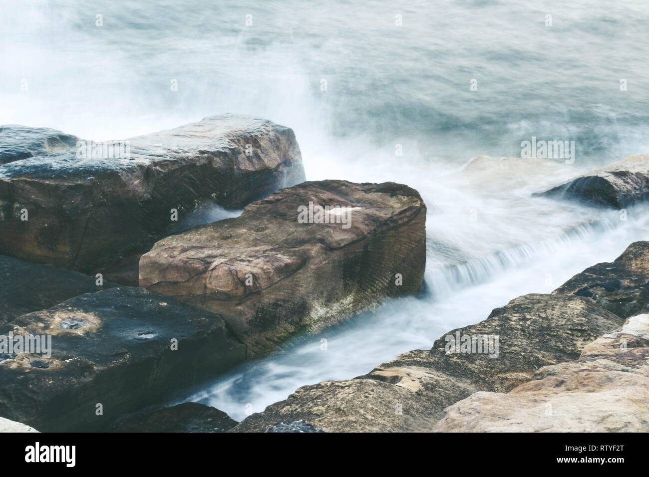 Una lunga esposizione di Sydney Harbour di acqua che scorre sulle rocce a Barangaroo Foto Stock