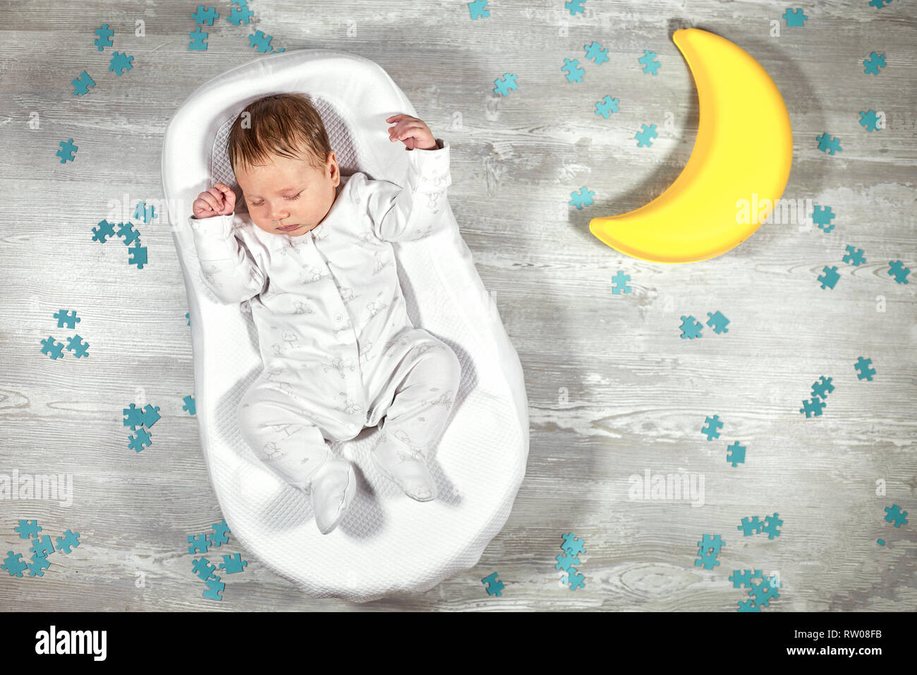 Neonato dorme in una speciale materasso ortopedico Baby cocoon, su un pavimento in legno, il giocattolo luna e puzzle intorno a. La calma e il sonno sano nei neonati. Foto Stock