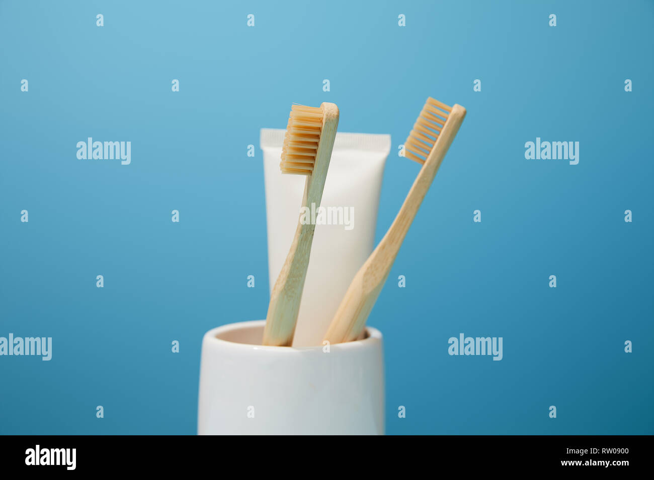 Titolare con il dentifricio nel tubo di bambù e di spazzolini da denti su sfondo blu Foto Stock