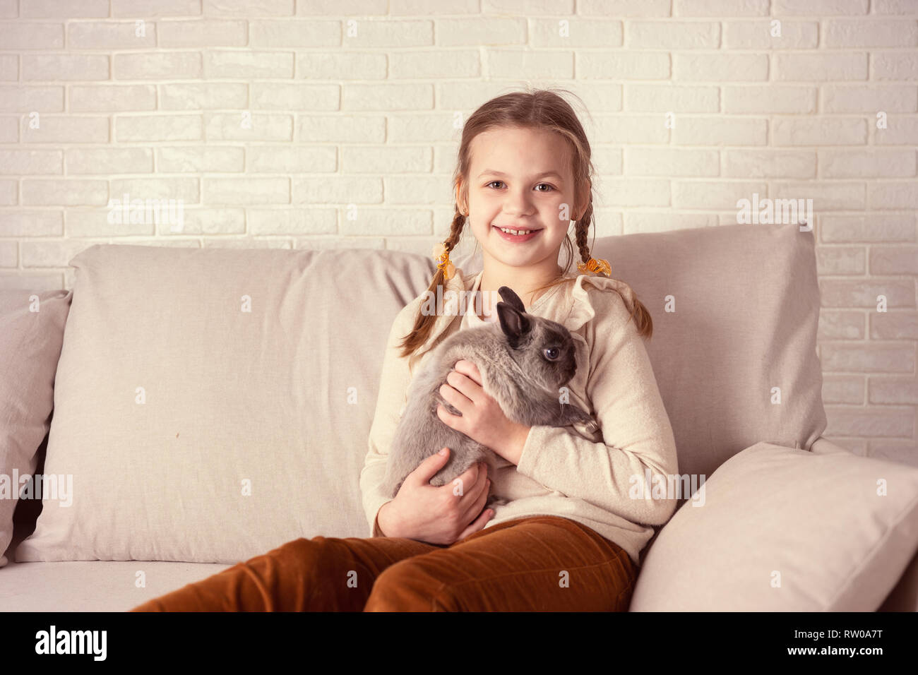 Ritratto di felice ragazza con coniglio sittiing sul divano nel soggiorno. Tonificazione rétro Foto Stock