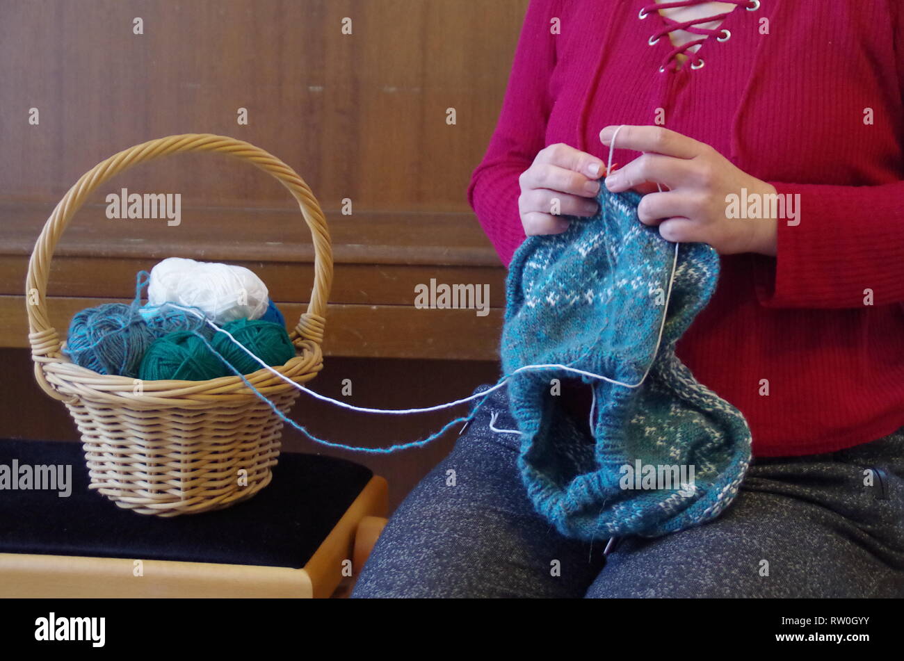 Una donna di lavorazione a maglia di un pullover con norewgian pattern e un cestello con palline di lana Foto Stock