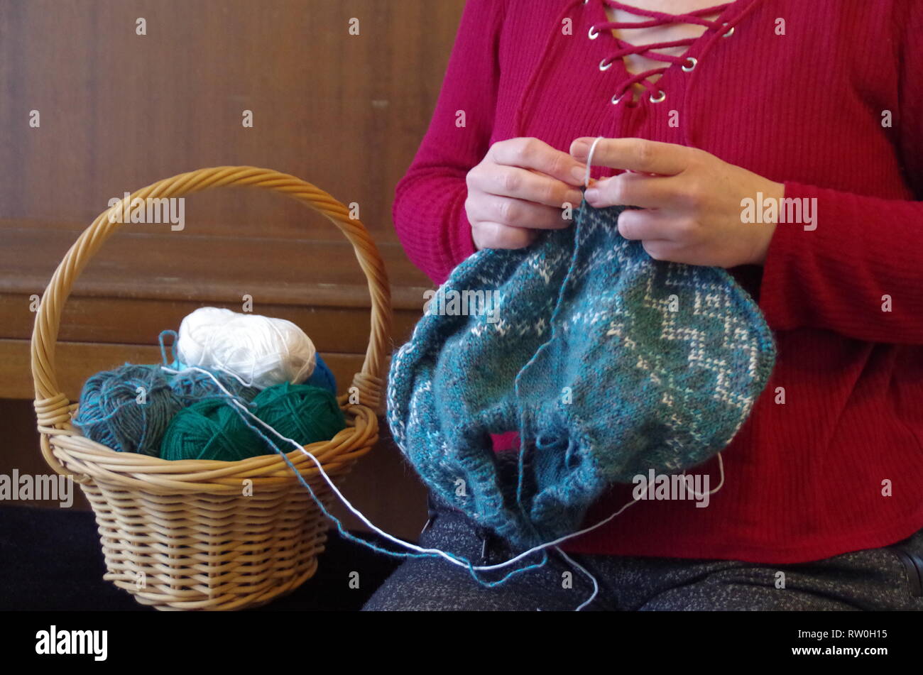 Una donna di lavorazione a maglia di un pullover con norewgian pattern e un cestello con palline di lana Foto Stock