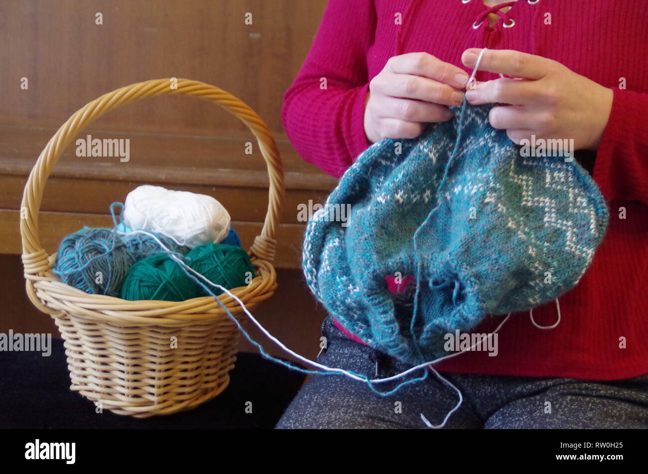 Una donna di lavorazione a maglia di un pullover con norewgian pattern e un cestello con palline di lana Foto Stock