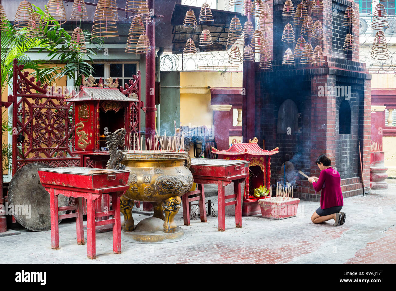 Peccato Sze Si Ya Tempio Taoista, Chinatown, Kuala Lumpur, Malesia. Adoratore inginocchiato con Joss (incenso) si inceppa nella parte anteriore del santuario. Foto Stock
