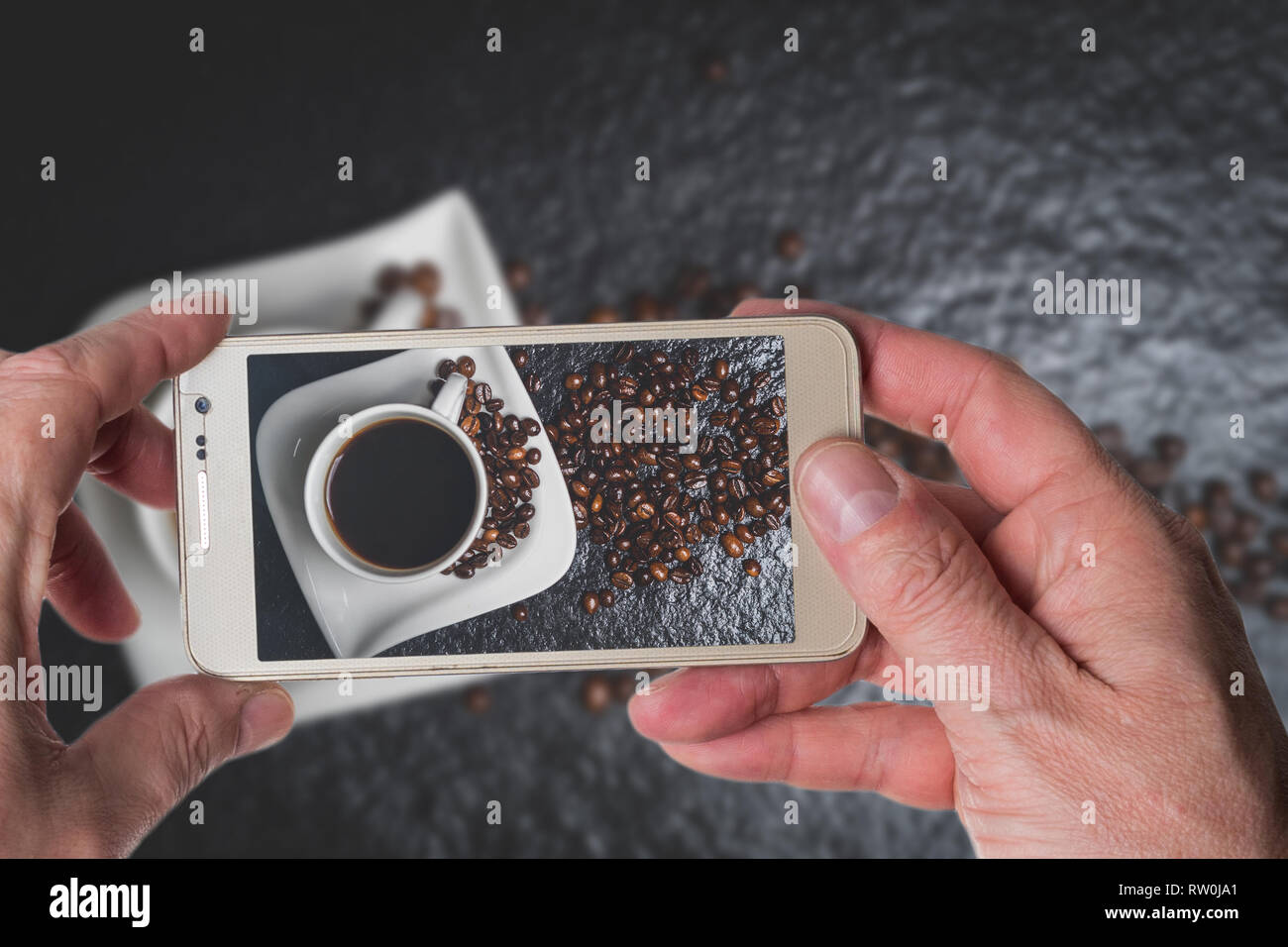 L'uomo prendendo foto di bianco tazza di caffè e chicchi di caffè nero sul tavolo in pietra vista superiore Foto Stock