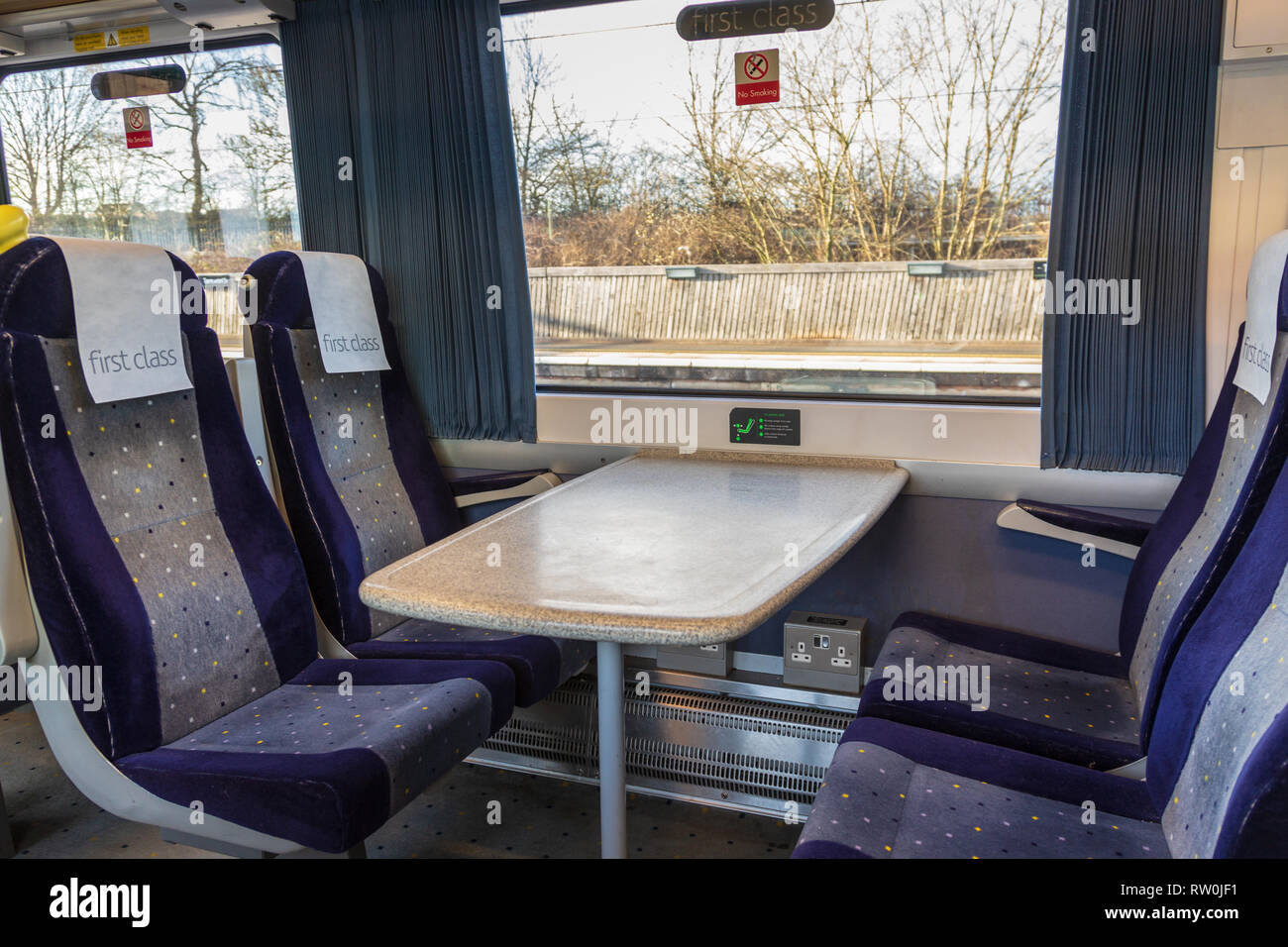 Prima classe seduta carrello vuoto su un treno. I quattro sedili blu e tabella sono accanto a una finestra con un primo segno di classe Foto Stock