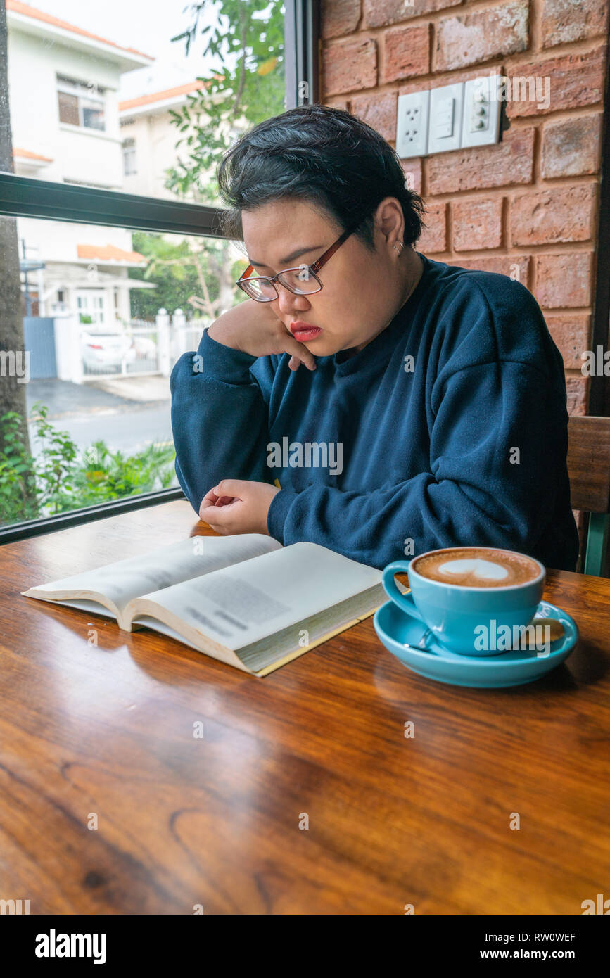 Foto verticale della ragazza asiatica la lettura di libri e di bere il caffè Foto Stock