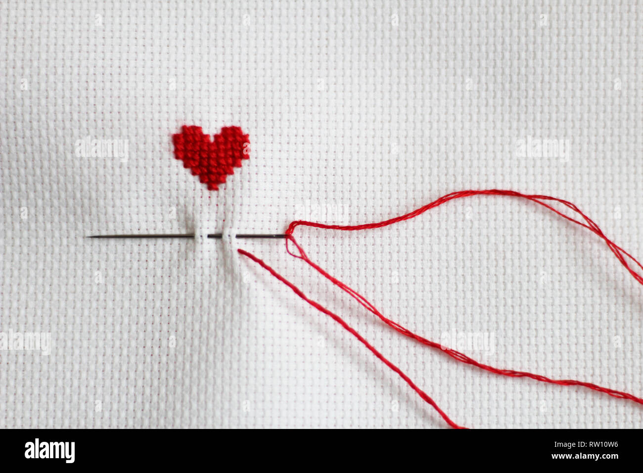 Ricamati a mano con cuore, ago, filo rosso, tela bianca Foto Stock