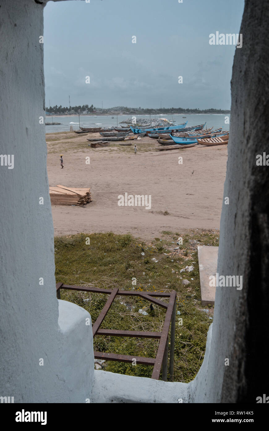 Una vista del paesaggio (spiaggia sabbiosa e vecchie barche di legno) che circonda il vecchio Elmina slave nel castello di Elmina, Ghana, Africa occidentale Foto Stock