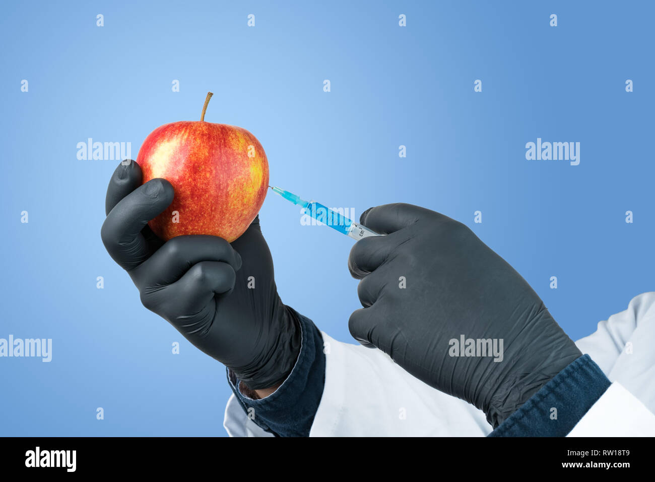 Ai giovani scienziati di iniettare il liquido di colore blu in un Apple su fondo azzurro. Alimenti geneticamente modificati ricerca concetto astratto. Foto Stock