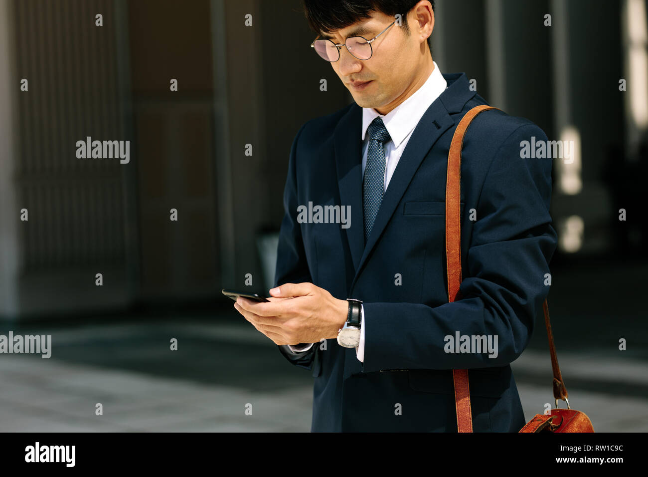 Imprenditore asiatici passeggiate all'aperto utilizzando il telefono cellulare. Il coreano uomo a camminare e utilizzando un telefono intelligente all'aperto. Foto Stock