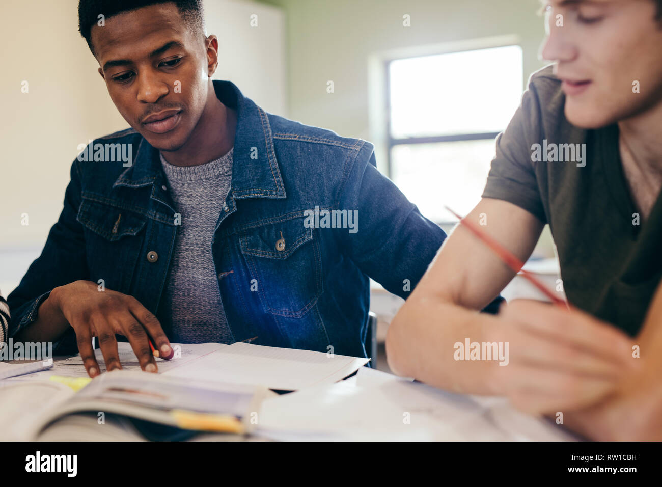 Gli studenti universitari che studiano con libri in biblioteca. I compagni di scuola seduti ad un tavolo e la lettura di libri di riferimento per il loro progetto. Foto Stock